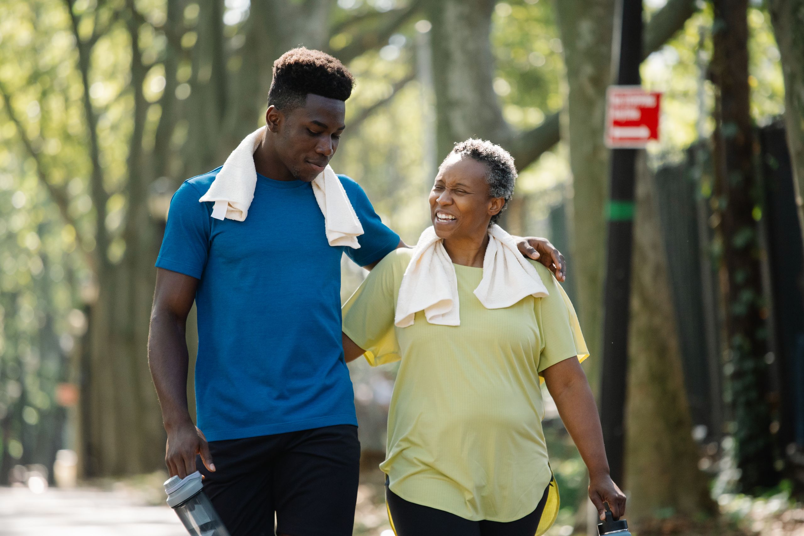 An elderly woman and young man walk arm in arm, smiling in a park. Active lifestyle.