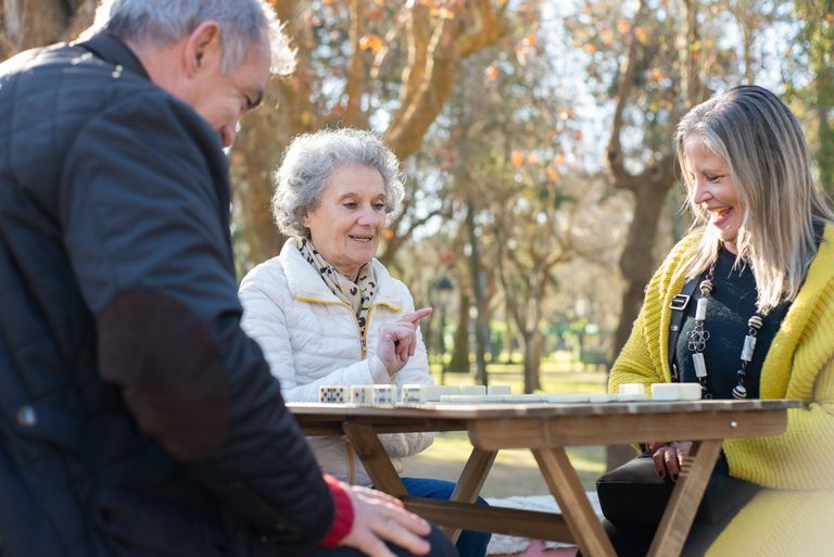 Elderly friends playing dominoes at a park in Portugal, outdoors and enjoying leisure time.