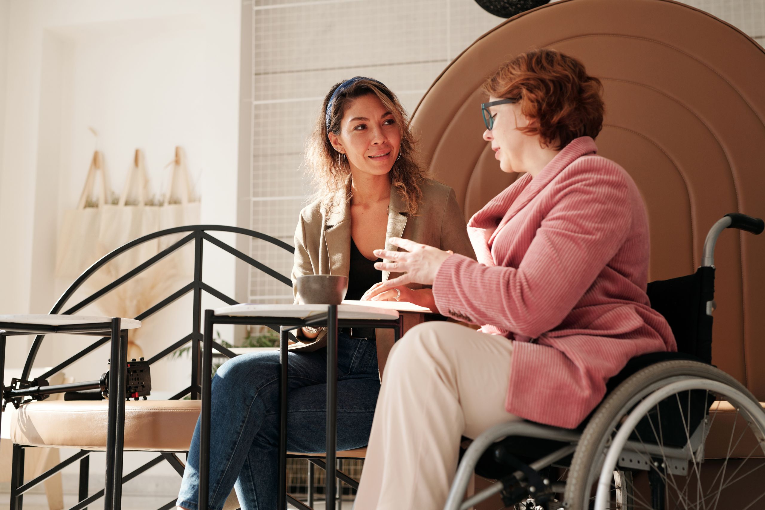 Two women in a café, one in a wheelchair, sharing a conversation.