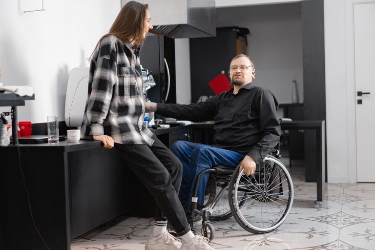 A man in a wheelchair and a woman conversing in a sleek, modern kitchen.
