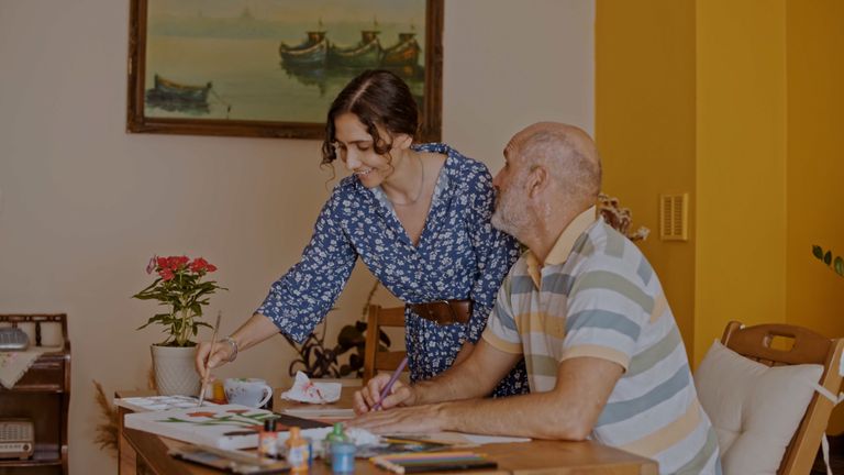 An elderly man and a woman enjoy a painting session together at a cozy indoor setting.