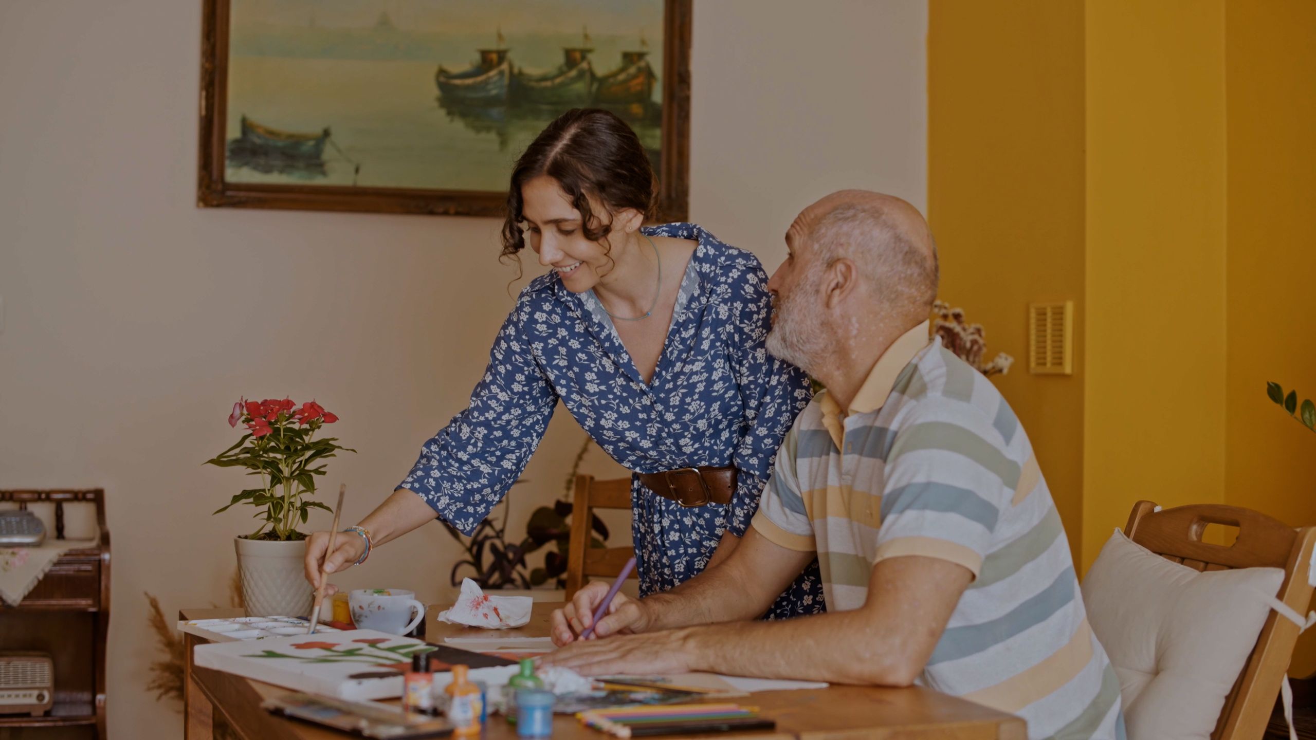An elderly man and a woman enjoy a painting session together at a cozy indoor setting.